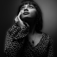 A vintage Hurrell style portrait of a woman in a blouse looking up with her right hand on her face in monochrome