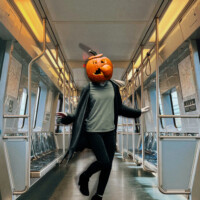 A woman with a pumpkin head standing in an empty train car.